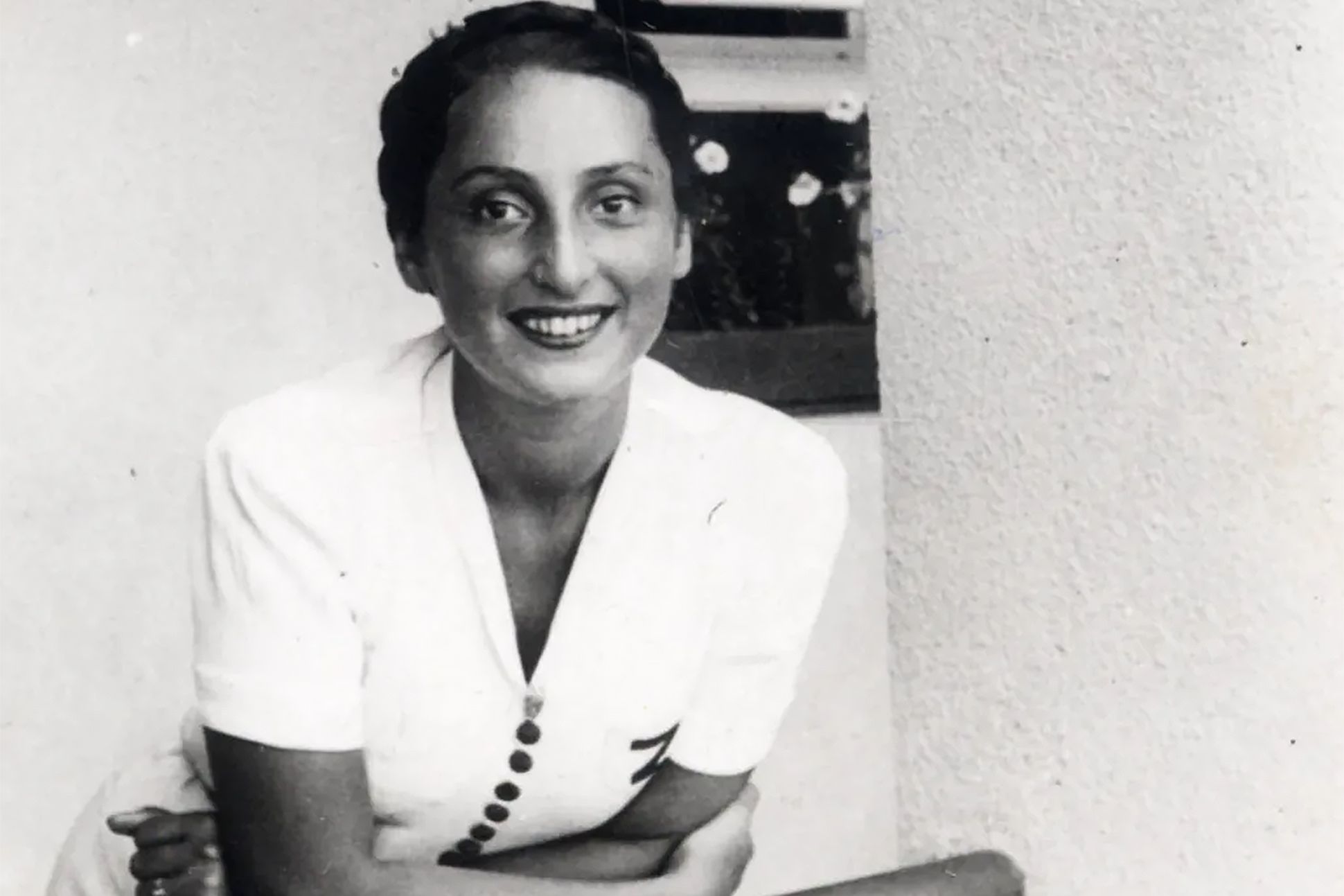 A black-and-white portrait of Zuzanna Ginczanka leaning against a balcony railing.