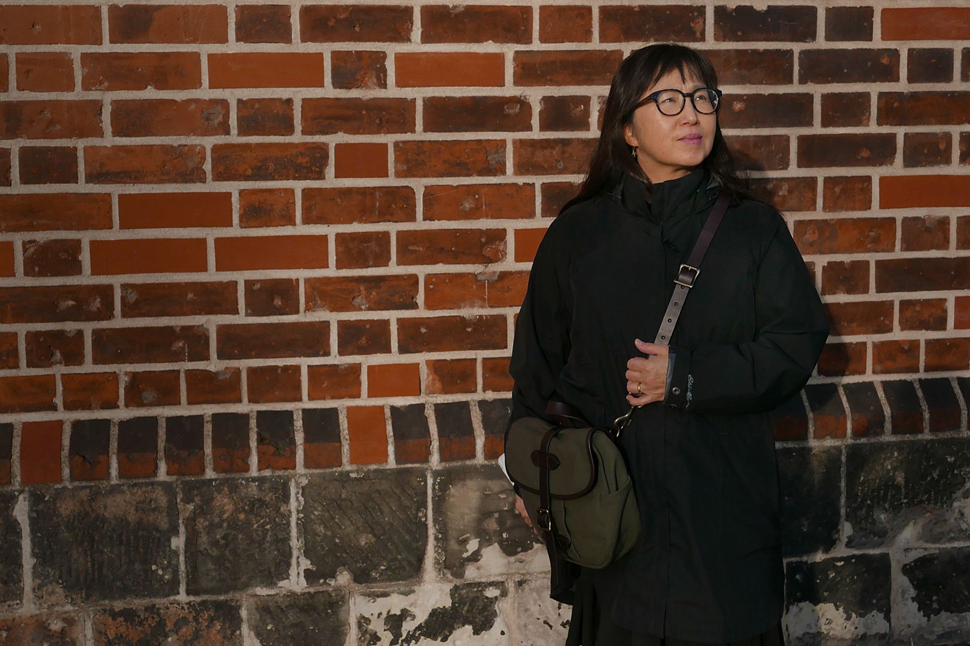 Portrait of Don Mee Choi standing against a brick wall.