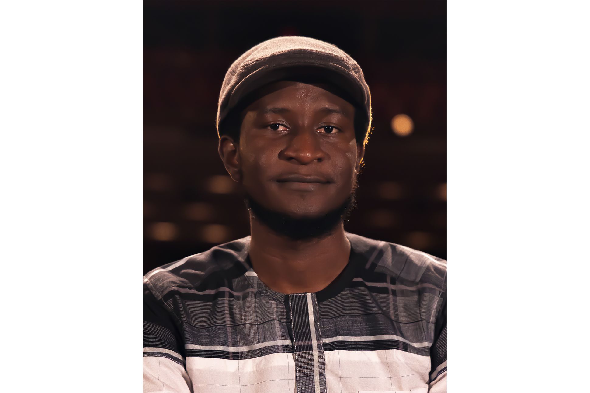 Poet Saddiq Dzukogi in a newsboy cap and plaid shirt with a dark starry background