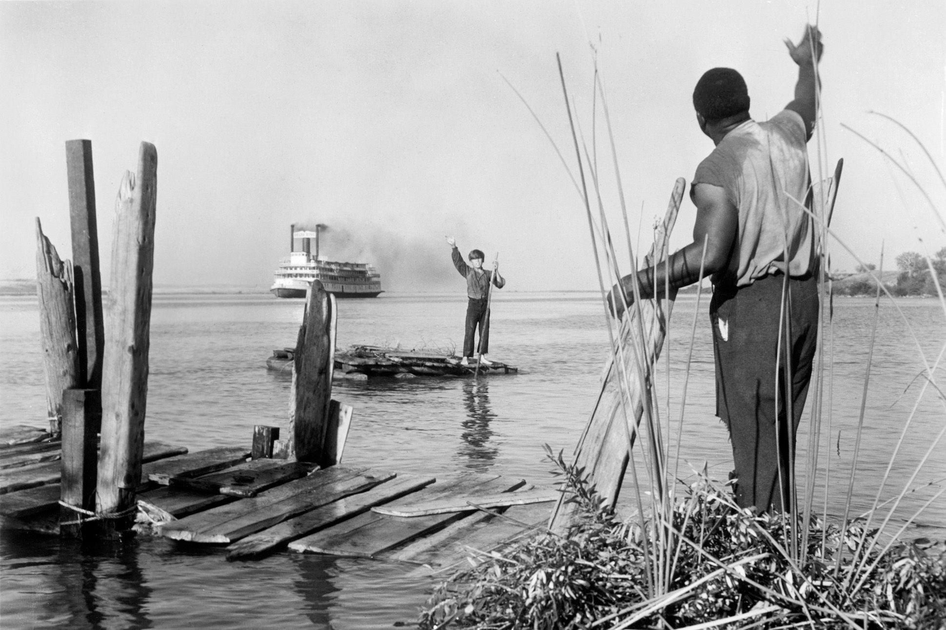 Publicity still of Archie Moore (1916 - 1998) waving to Huck while steamboat passes in the film 'The Adventures of Huckleberry Finn' (MGM), 1960.