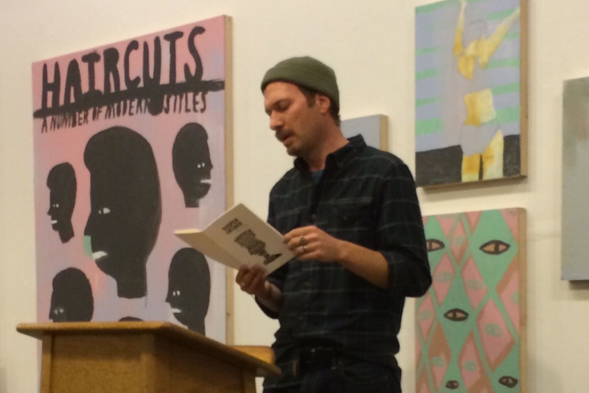 Man in a beanie reading in front of paintings