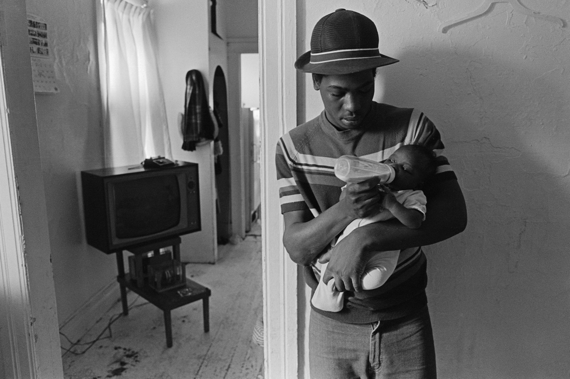 Black-and-white photo of a Black father bottle-feeding a baby.