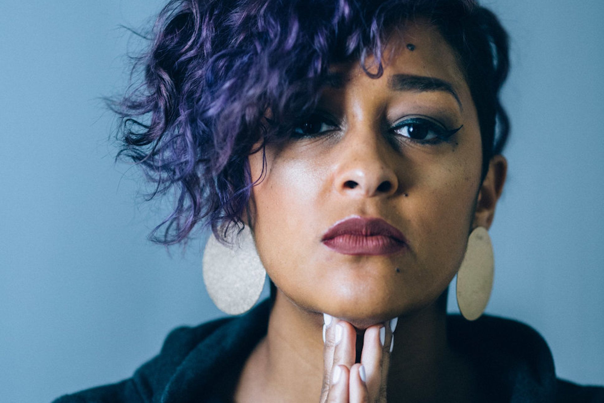 Close-up portrait of poet Eve Ewing with hands clasped together.