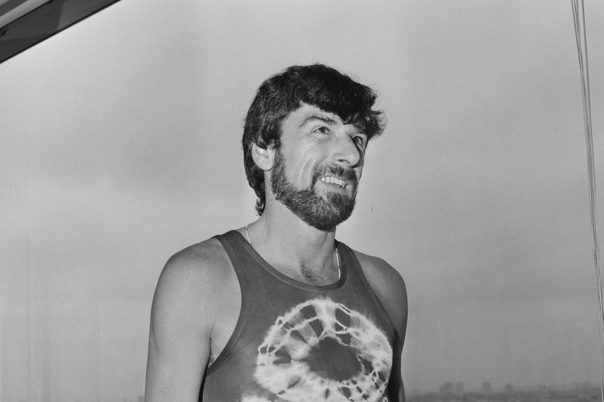 Black-and-white portrait of Thom Gunn standing and smiling.