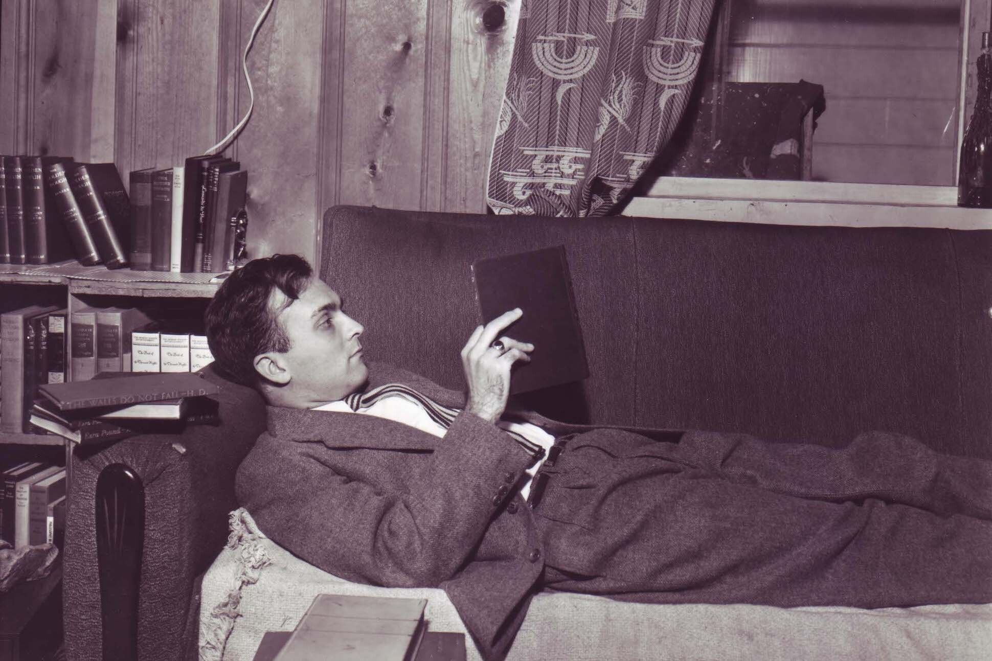 Photo of Robert Duncan reading while reclining on soda