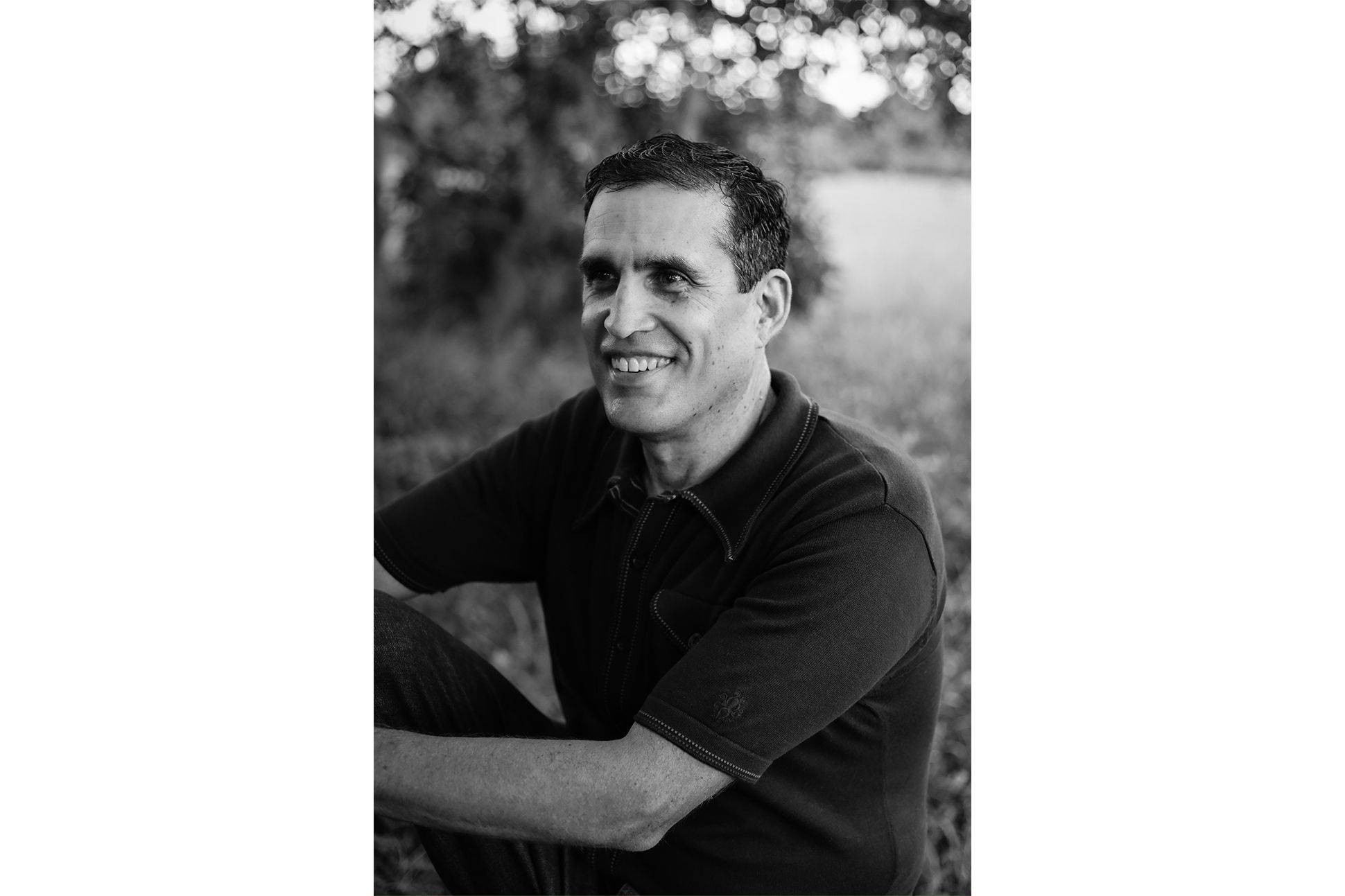 Black and white portrait of a white man in polo shirt sitting and smiling by a river