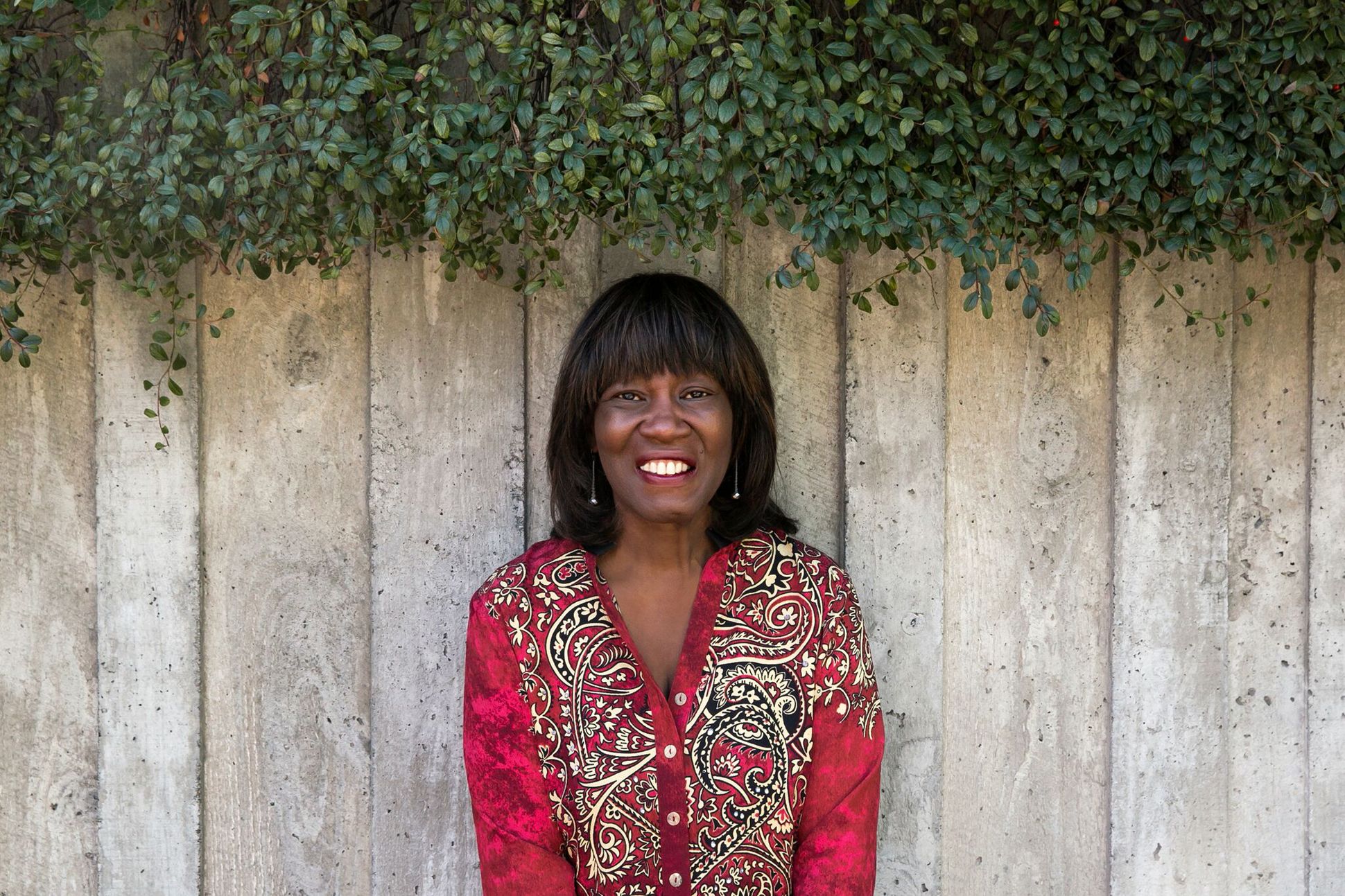Poet Patricia Smith poses in front of a wooden fence, wearing a bright red shirt.