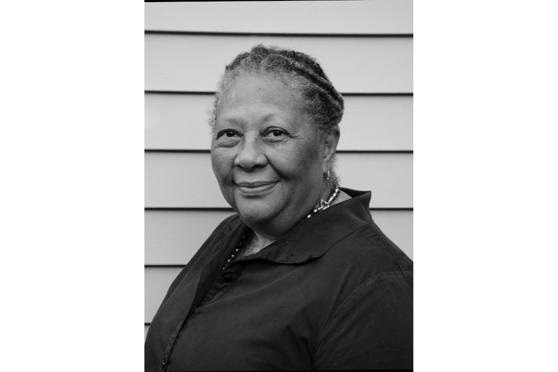 Black and white portrait of Marilyn Nelson in a shirt with a fenced background