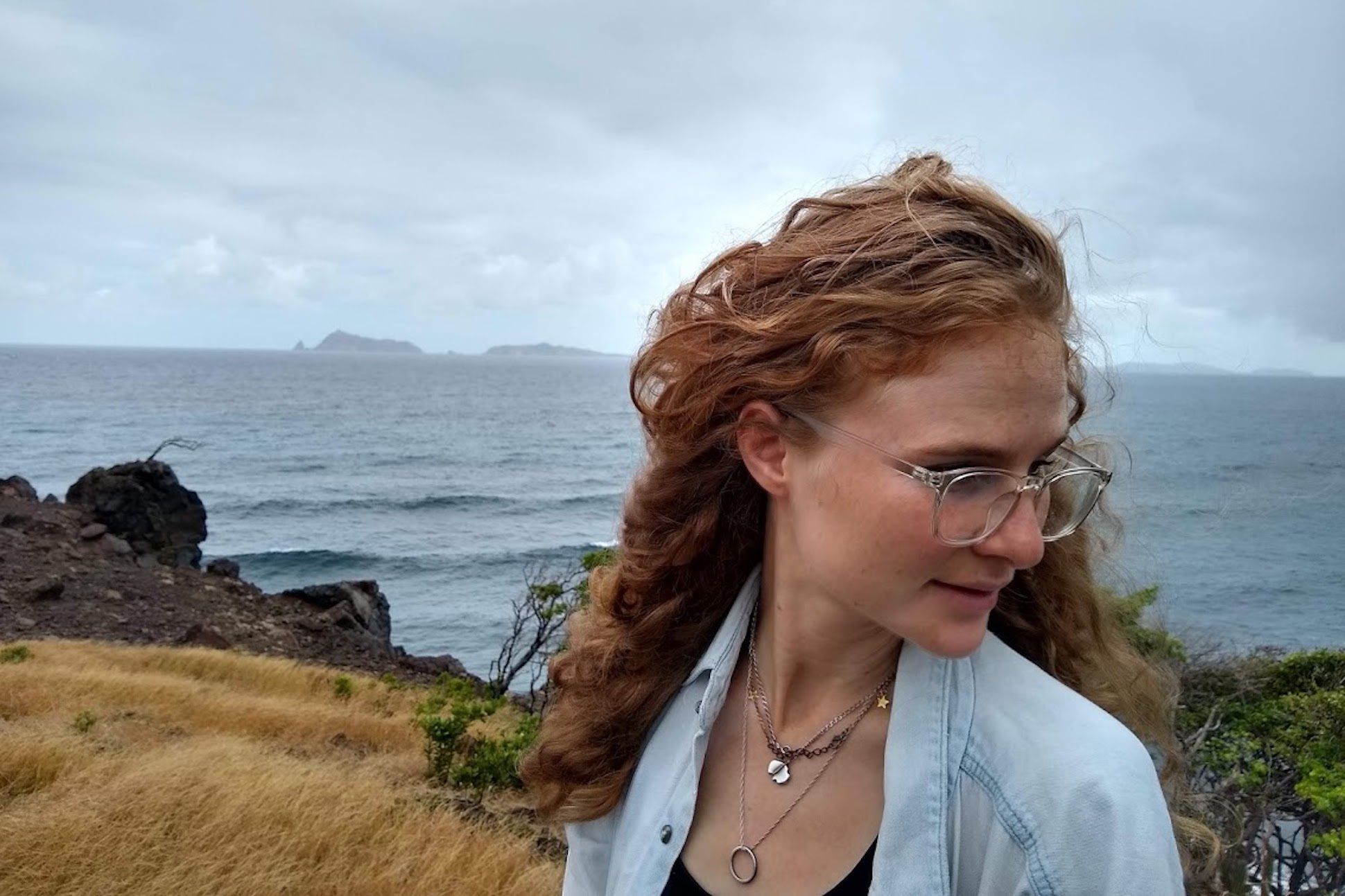 A white woman with long ginger hair having her head turned from the sea