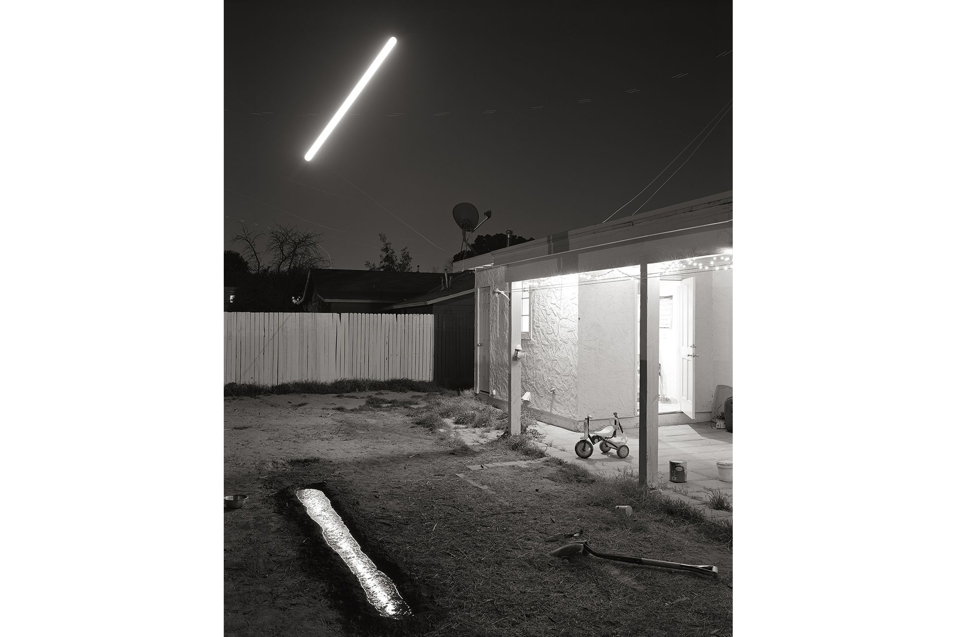 David Shannon-Lier, "Reflection of the Rising Moon Over Our Home, Mesa, Arizona. 2014." Backyard with fluorescent tube light hanging from the sky.