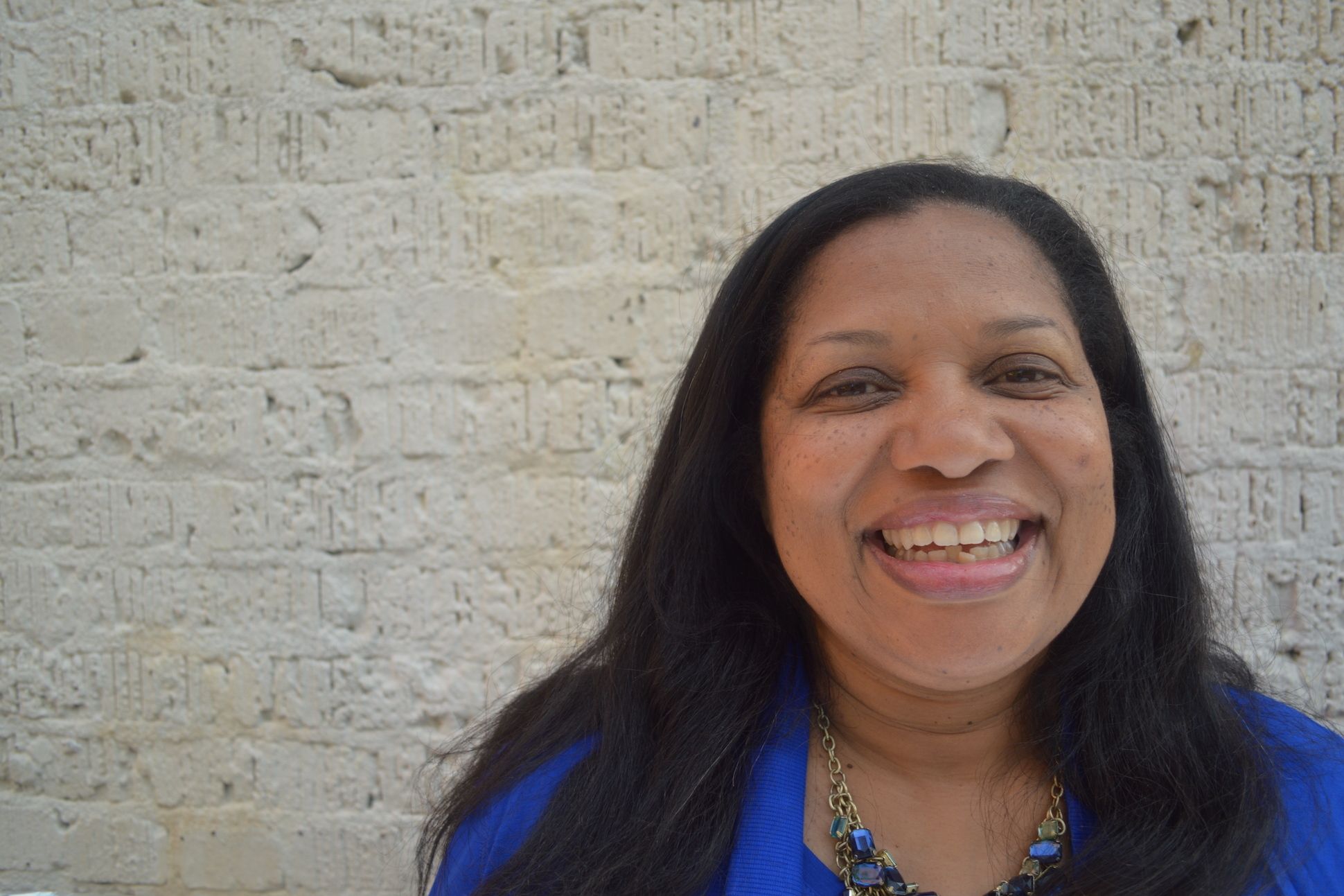 A woman in a blue top smiling in front of a brick wall