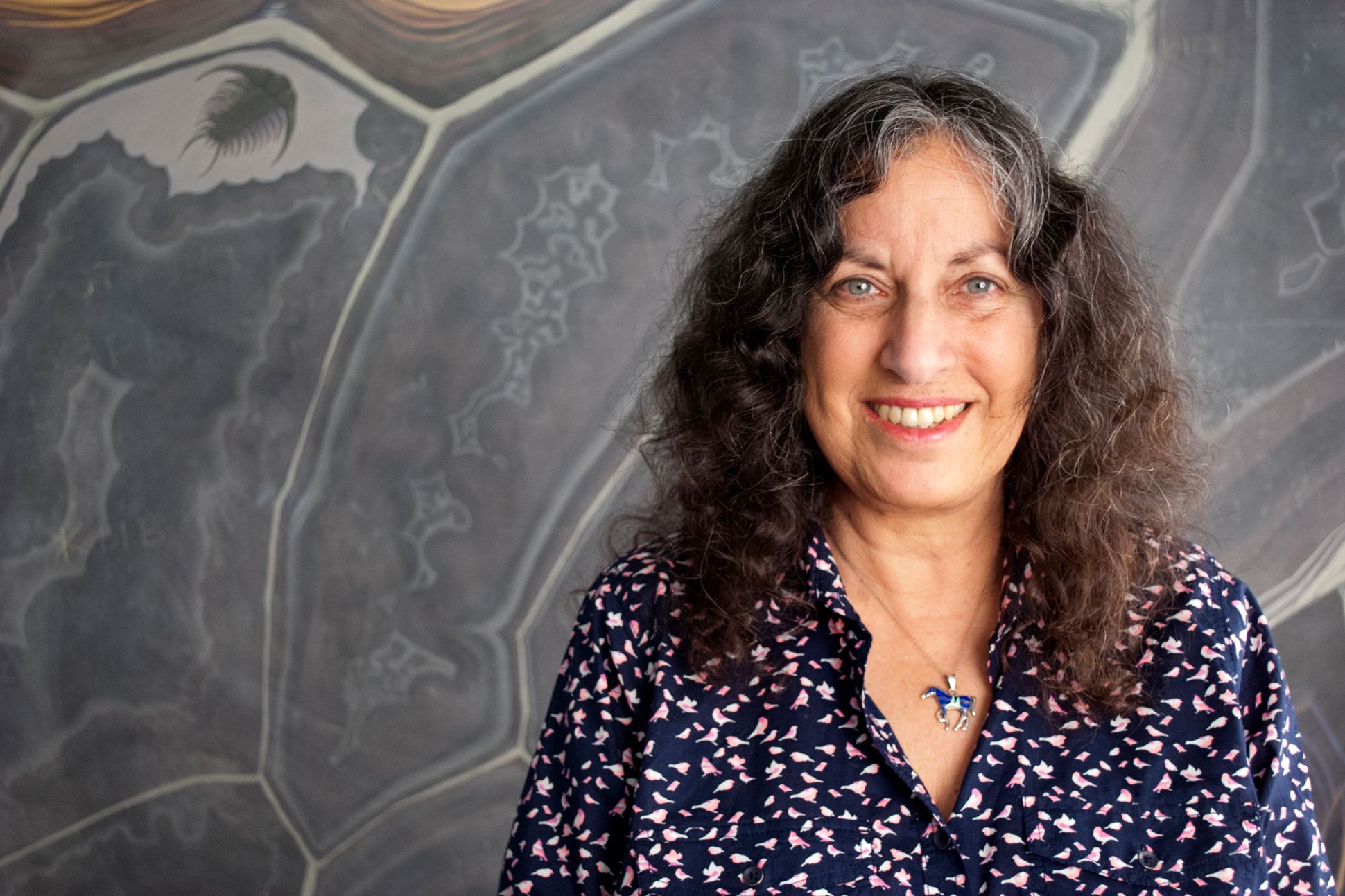 Poet Margarita Engle poses in a dark blue shirt and pink, wearing a horse necklace.
