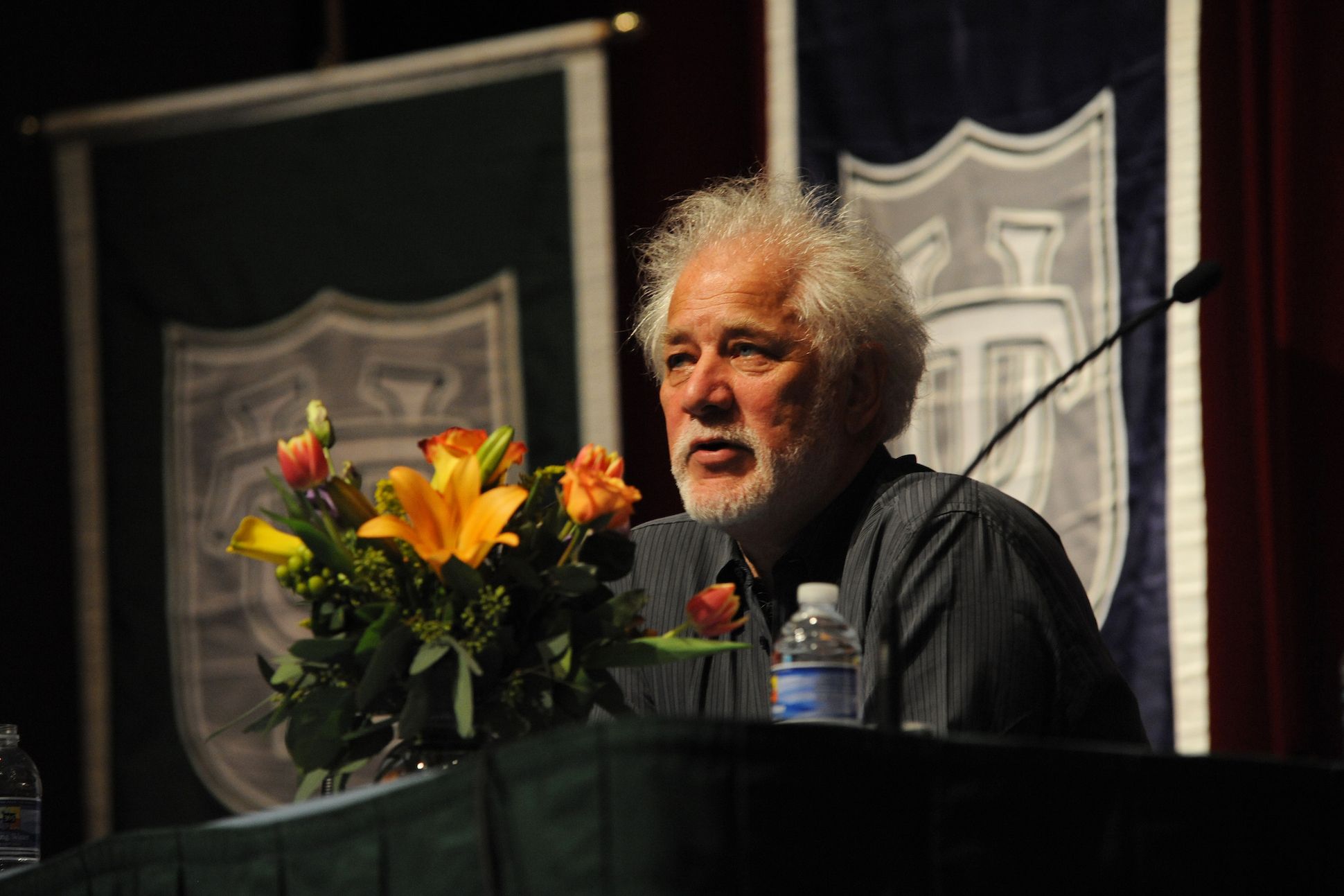 Headshot of poet Michael Ondaatje giving out a speech on a stage