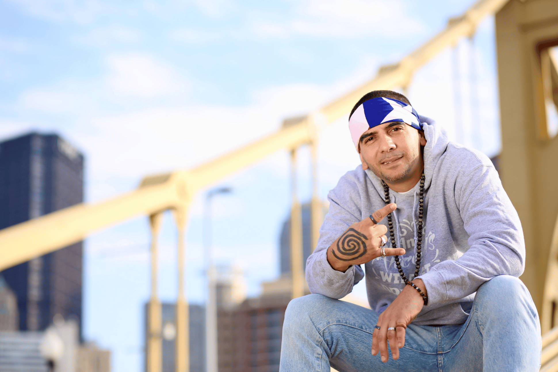 A white man in a headband posing in front of a bridge