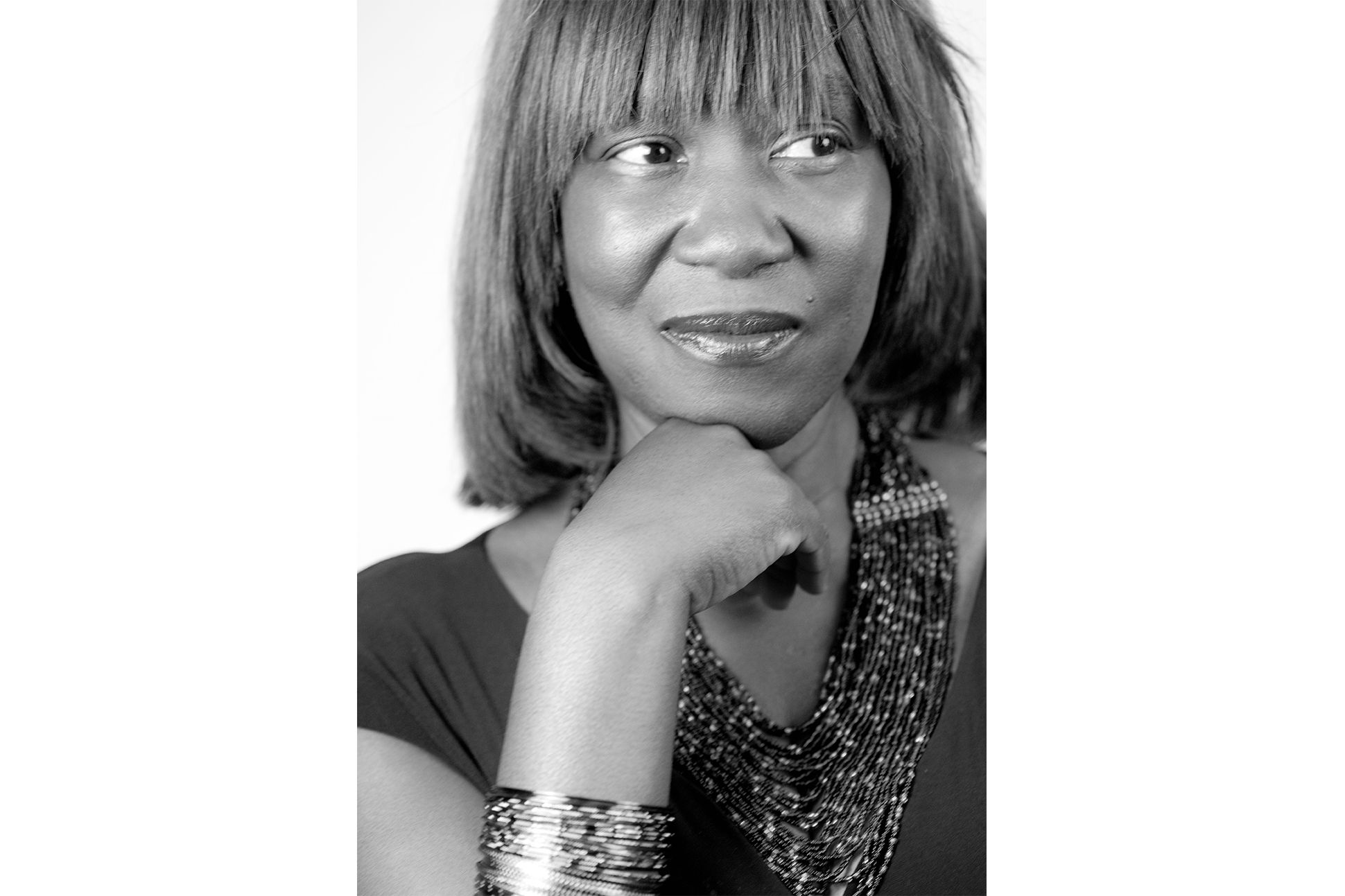 Poet Patricia Smith wearing a beaded necklace and smiling with her hand on her chin