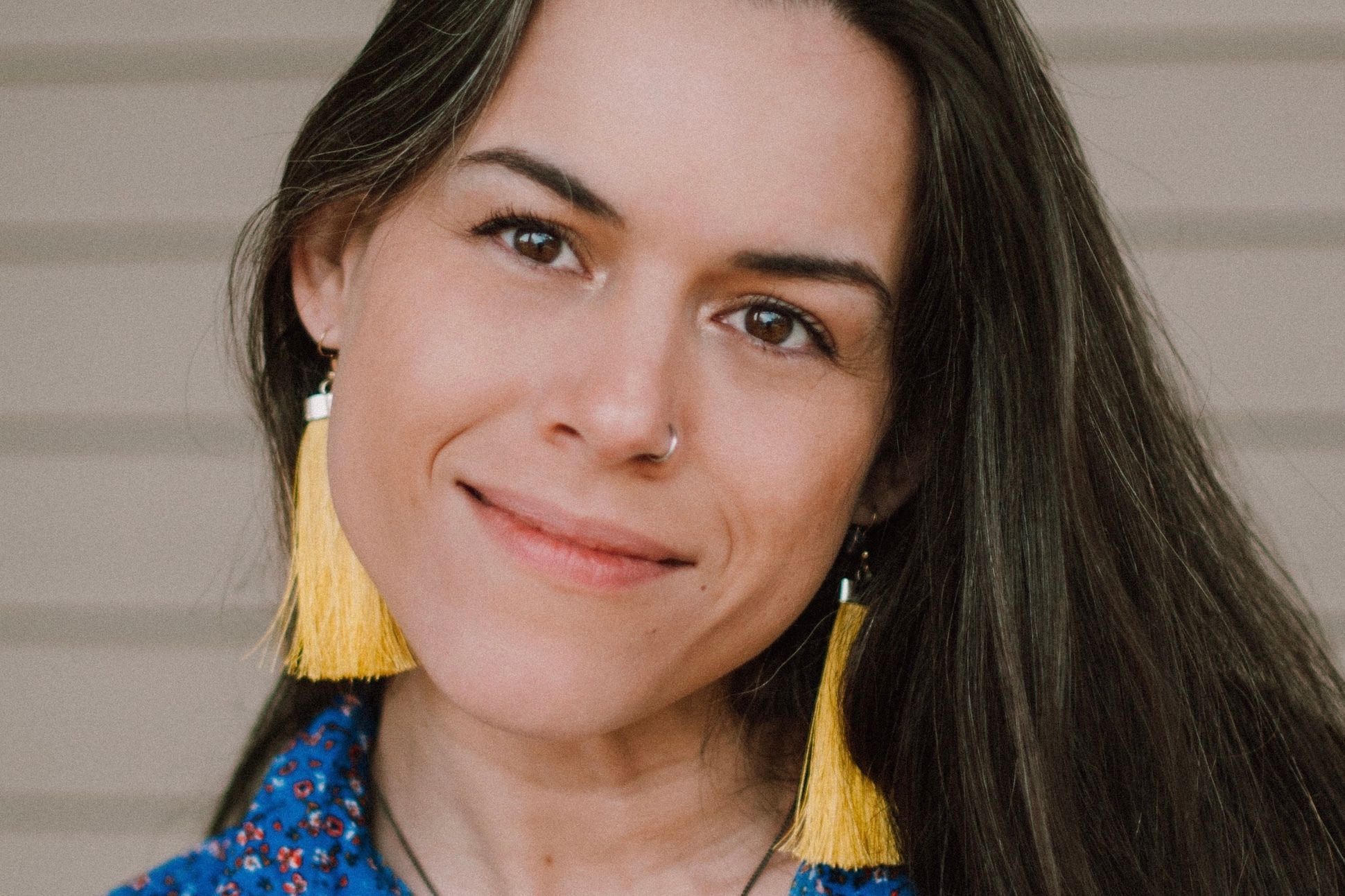 Woman with long hair and yellow tassel earrings smiling with her head tilted