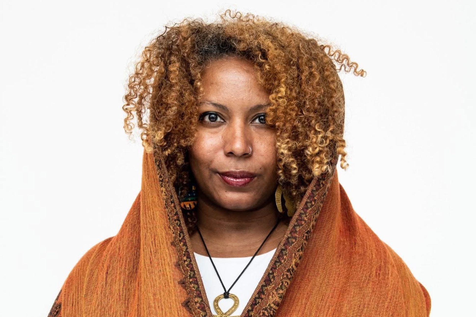 Faylita Hicks, an Afro-Latinx nonbinary femme person with goldfish-brown curly hair, wearing a honey-colored scarf.