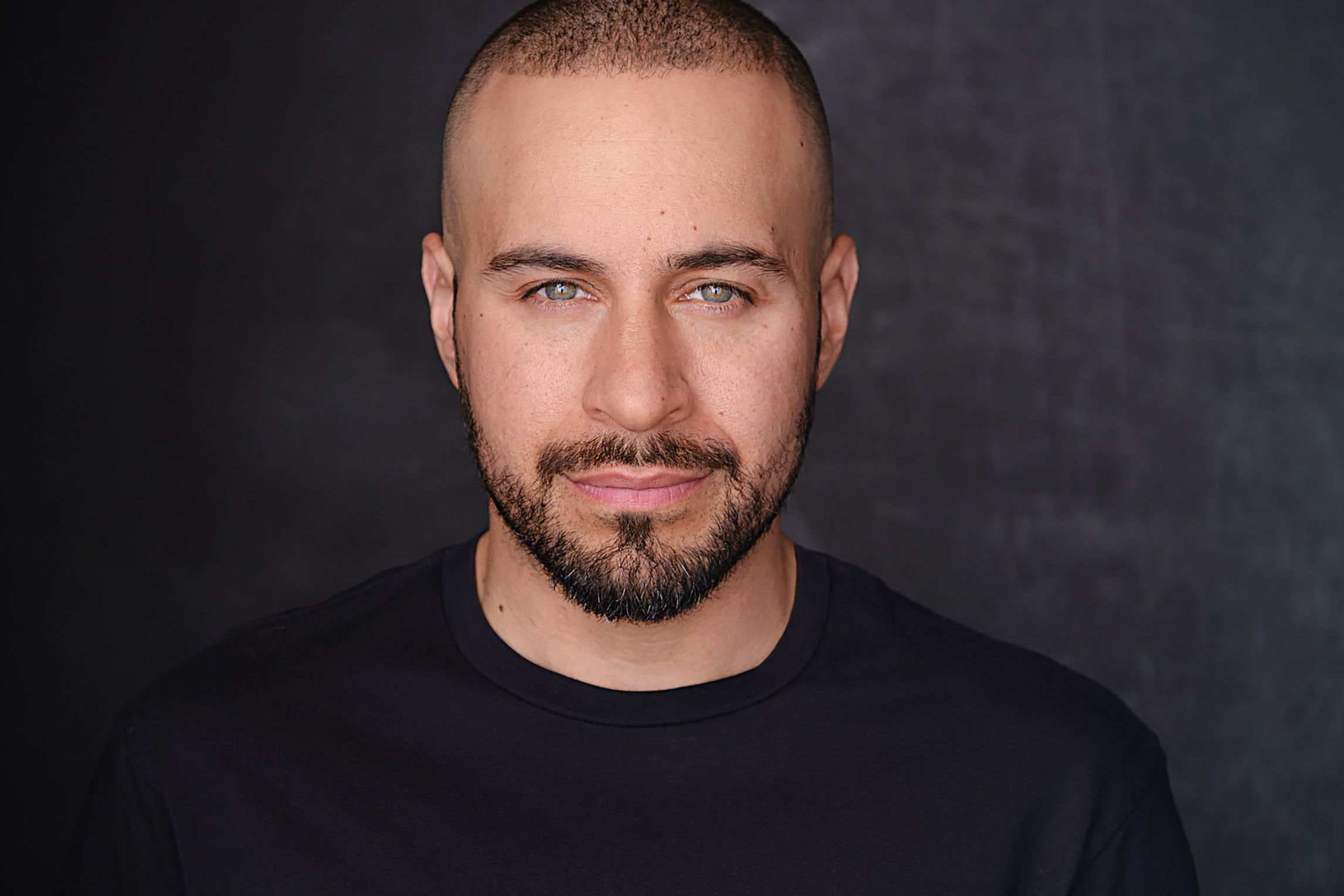 Luis Tubens, a Puerto Rican poet in a black shirt, looking straight ahead.