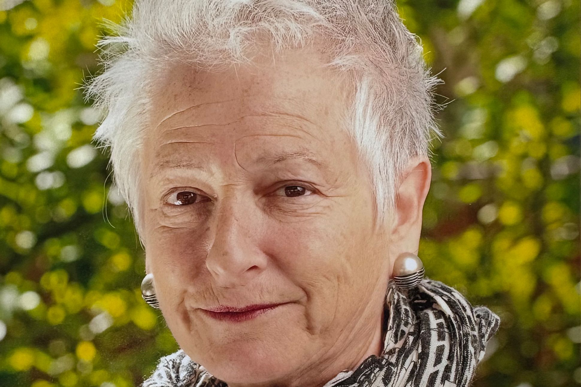 A closeup portrait of Robin Becker standing in front of greenery.
