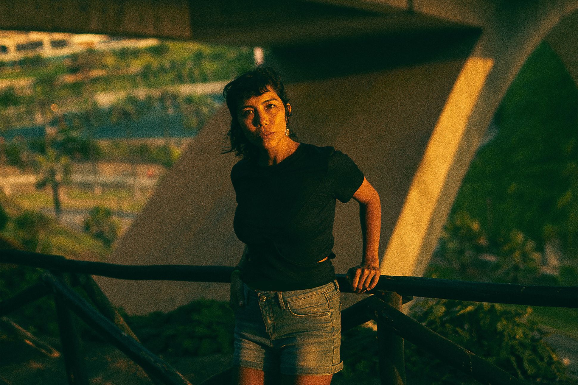 A photograph of Tilsa Otta in a black t-shirt and denim shorts standing against a rail outside.