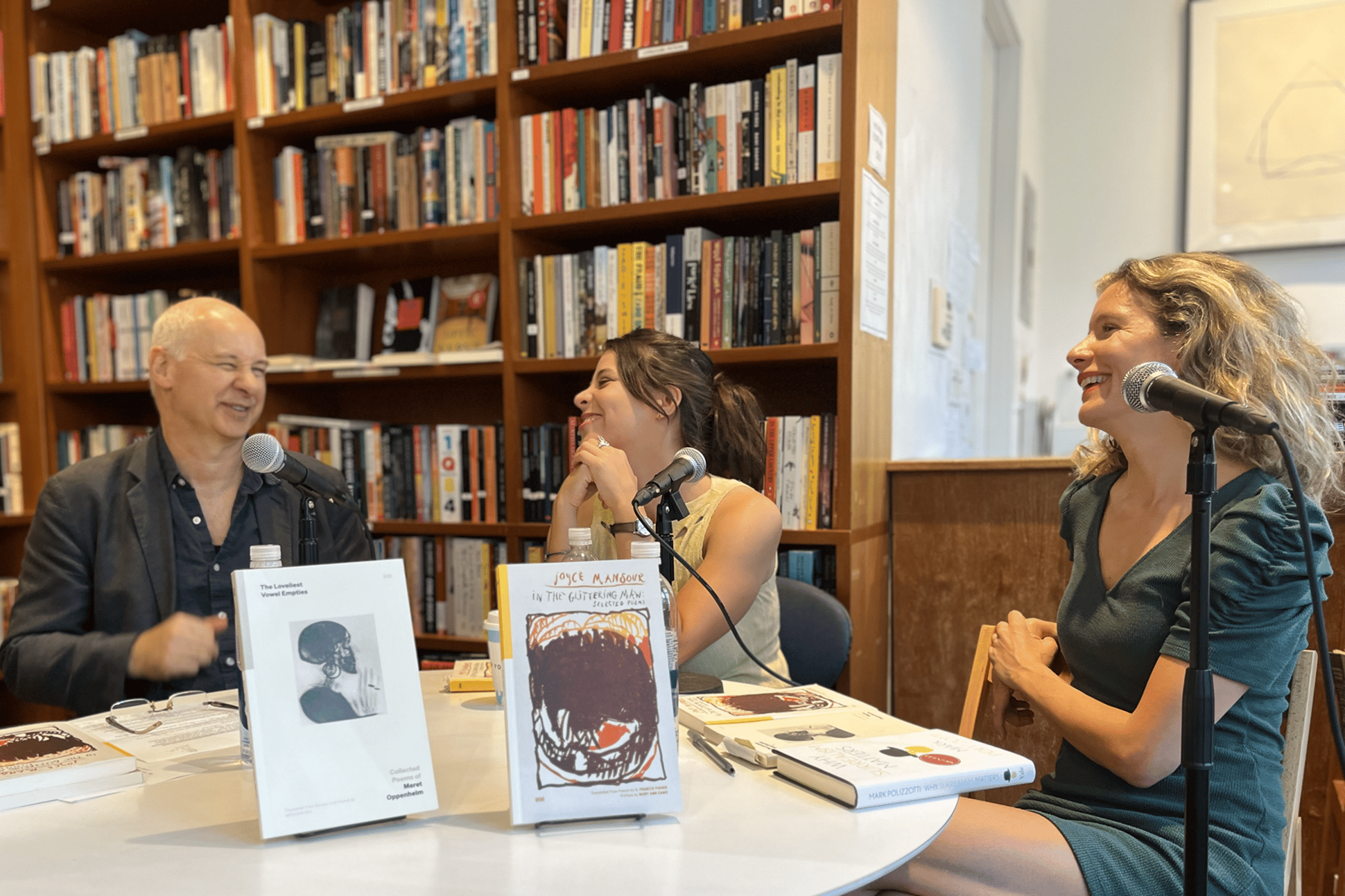 Three adults sitting at a table full of books, in conversation, with shelves of books behind them.