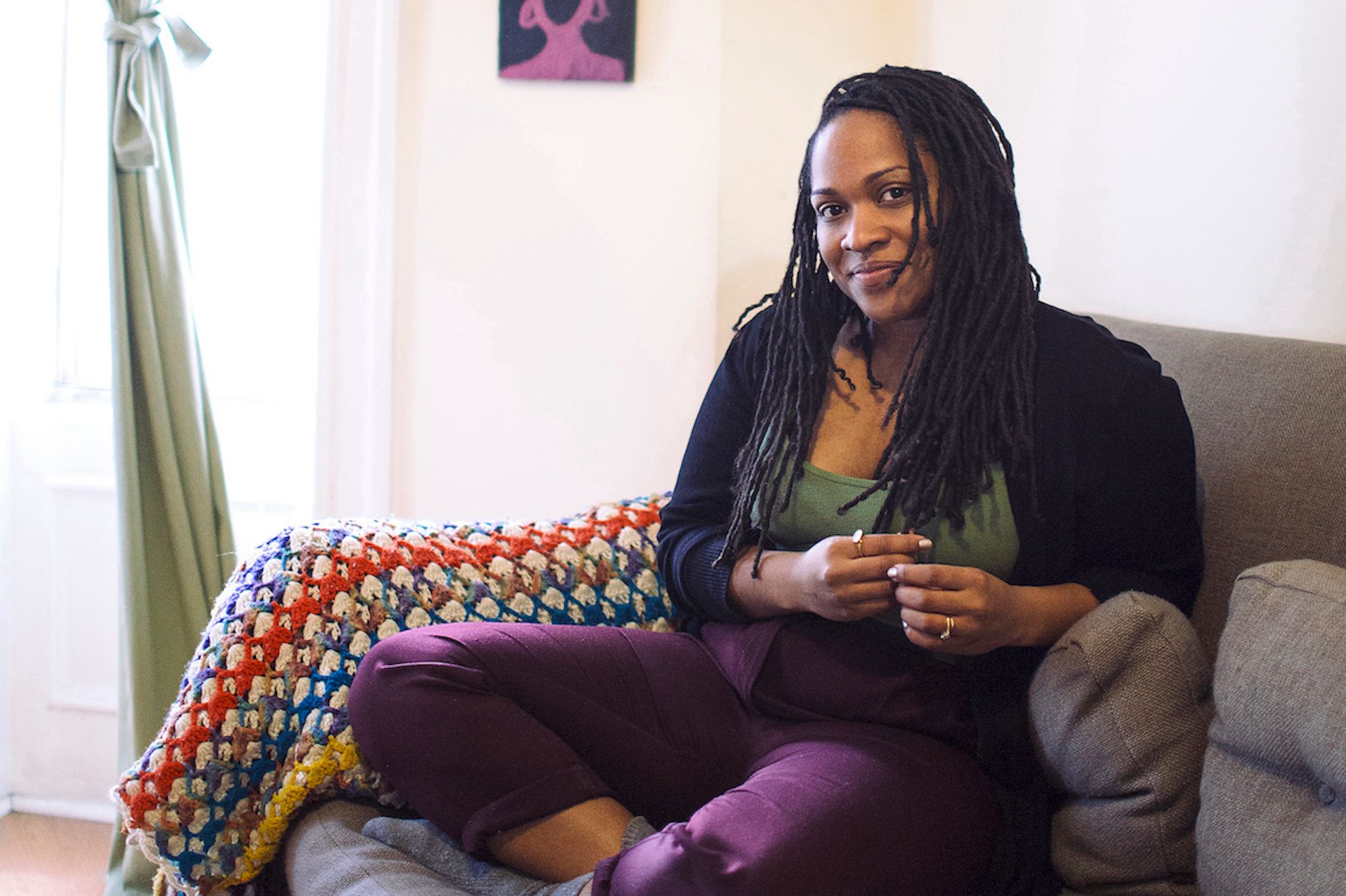 Black woman in a green top and purple pants sitting on a couch