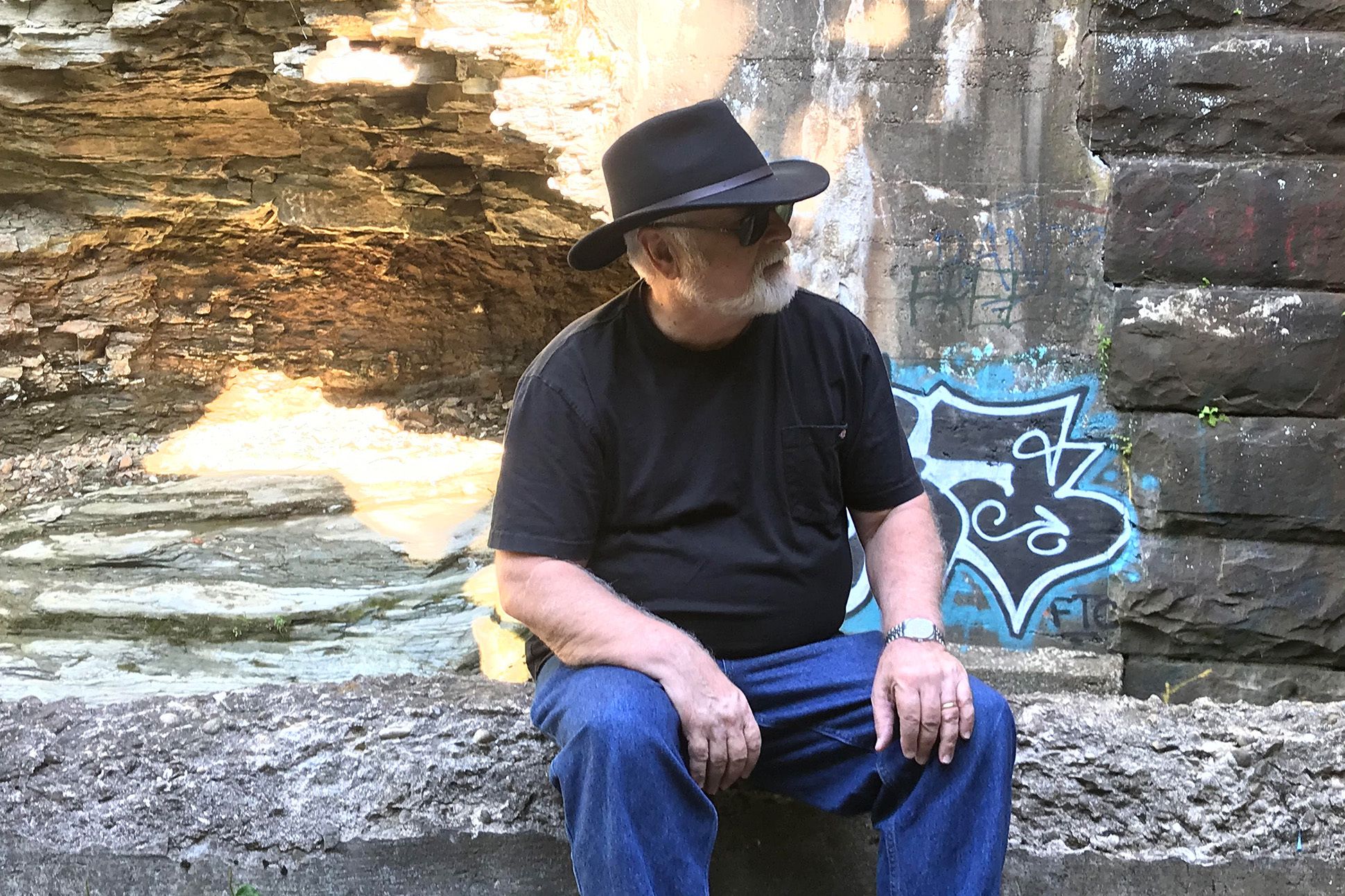 Poet Michael Simms sitting on a rock formation. Behind him is more rock formations with graffiti