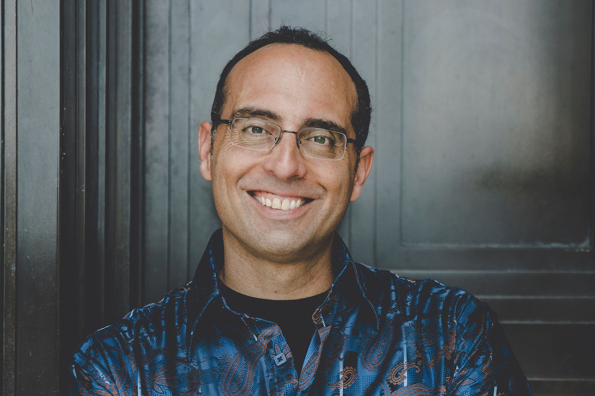Image of Philip Metres, a brown man with black hair, wearing dark blue and paisley shirt, with arms crossed