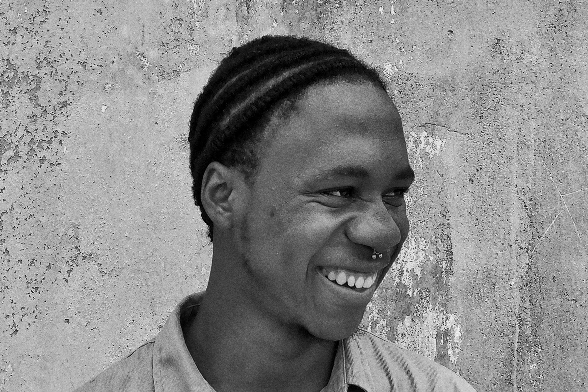 A black man with braided hair in front of a concrete wall