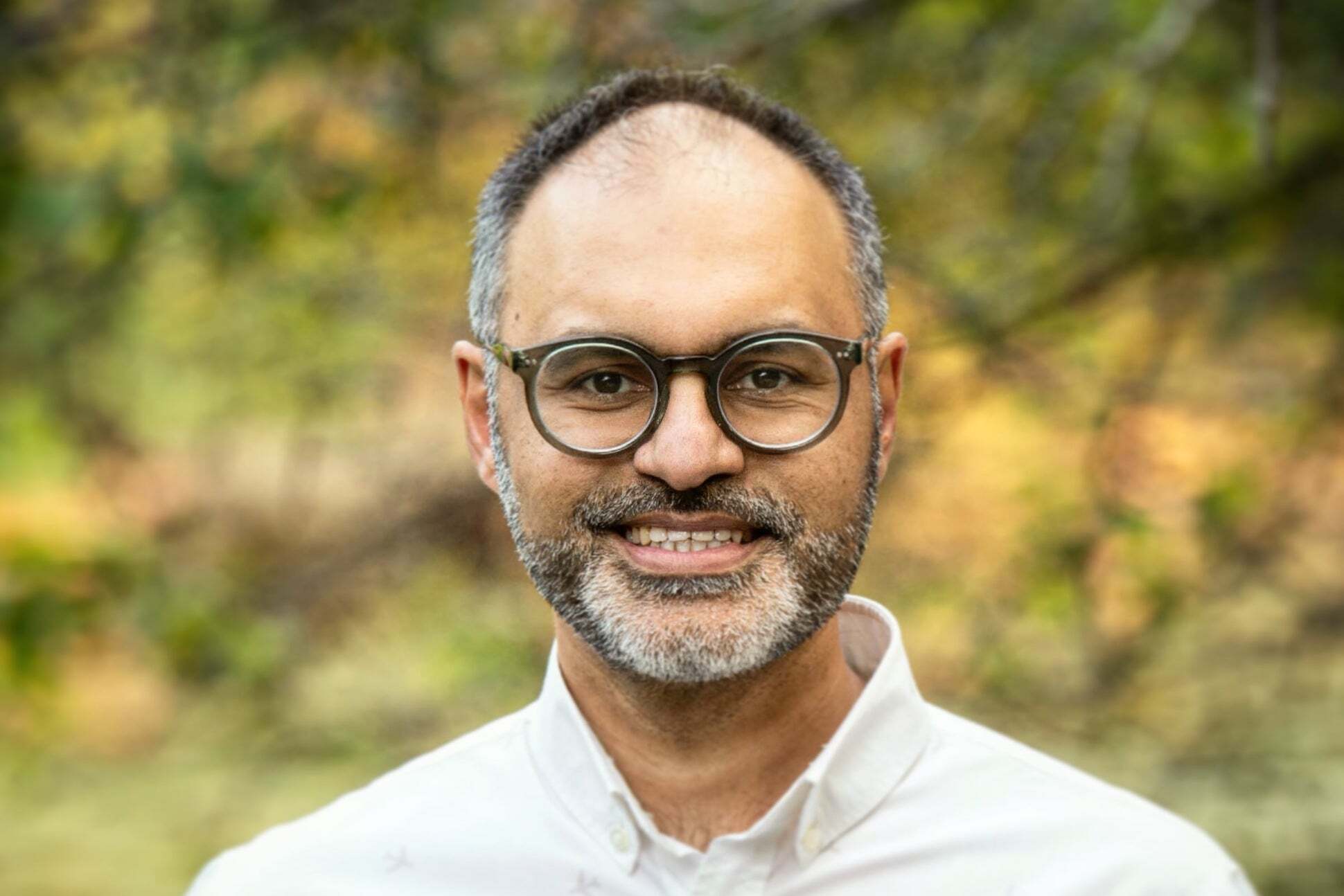 A white man with glasses and a white shirt smiling