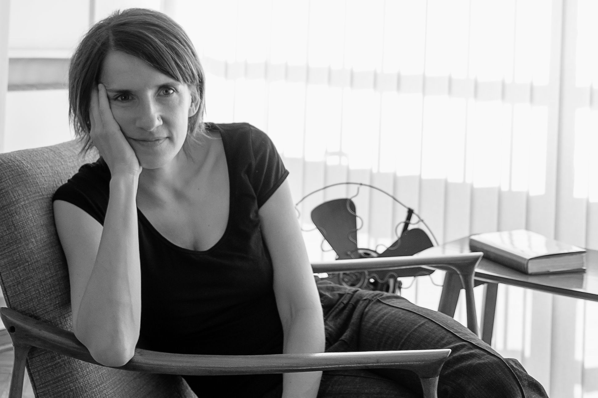 Black and white portrait of a short haired woman sitting on a lounge chair next to a fan