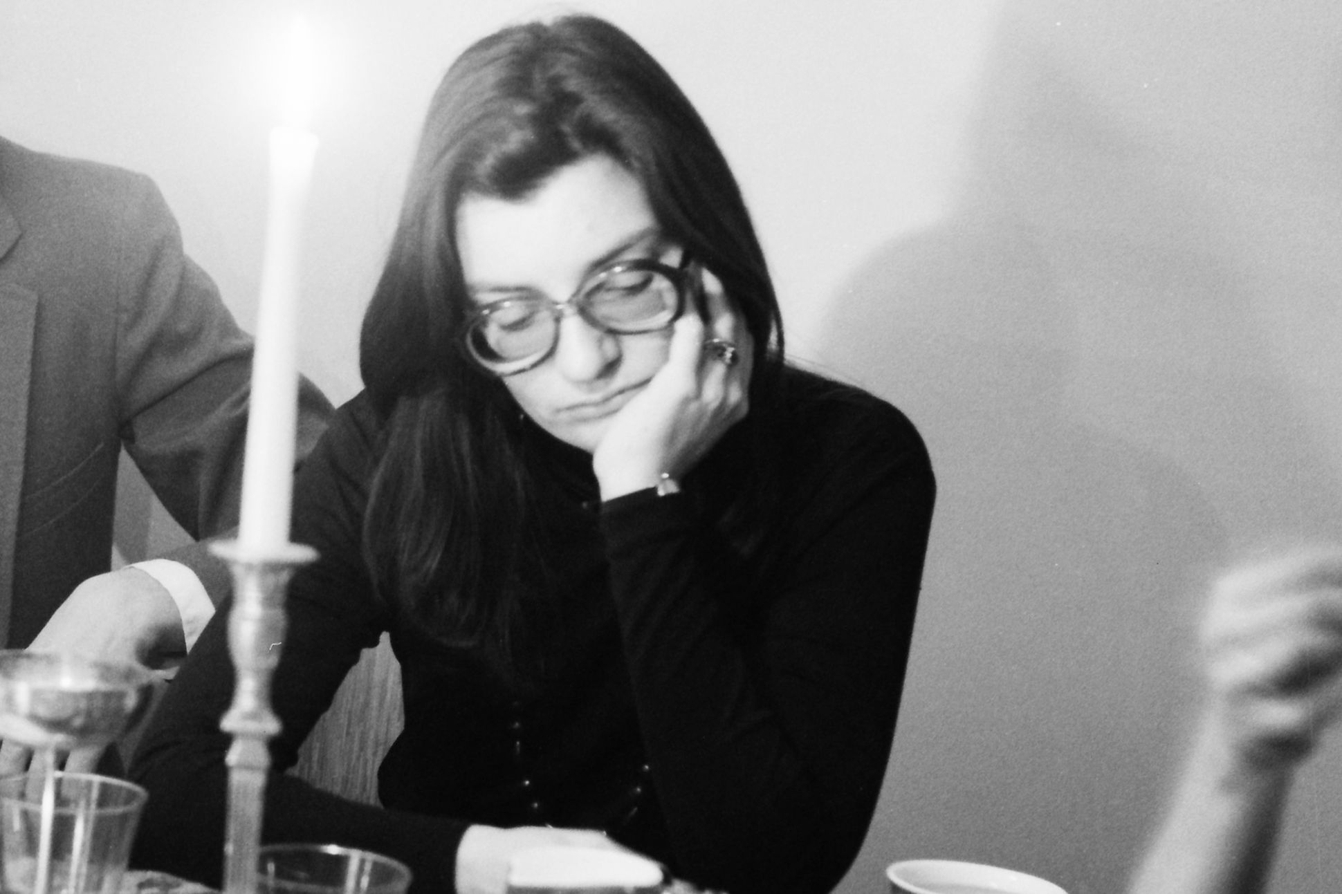 A black-and-white photo of Jane Kenyon sitting a table looking downward. A lit candle is nearby.