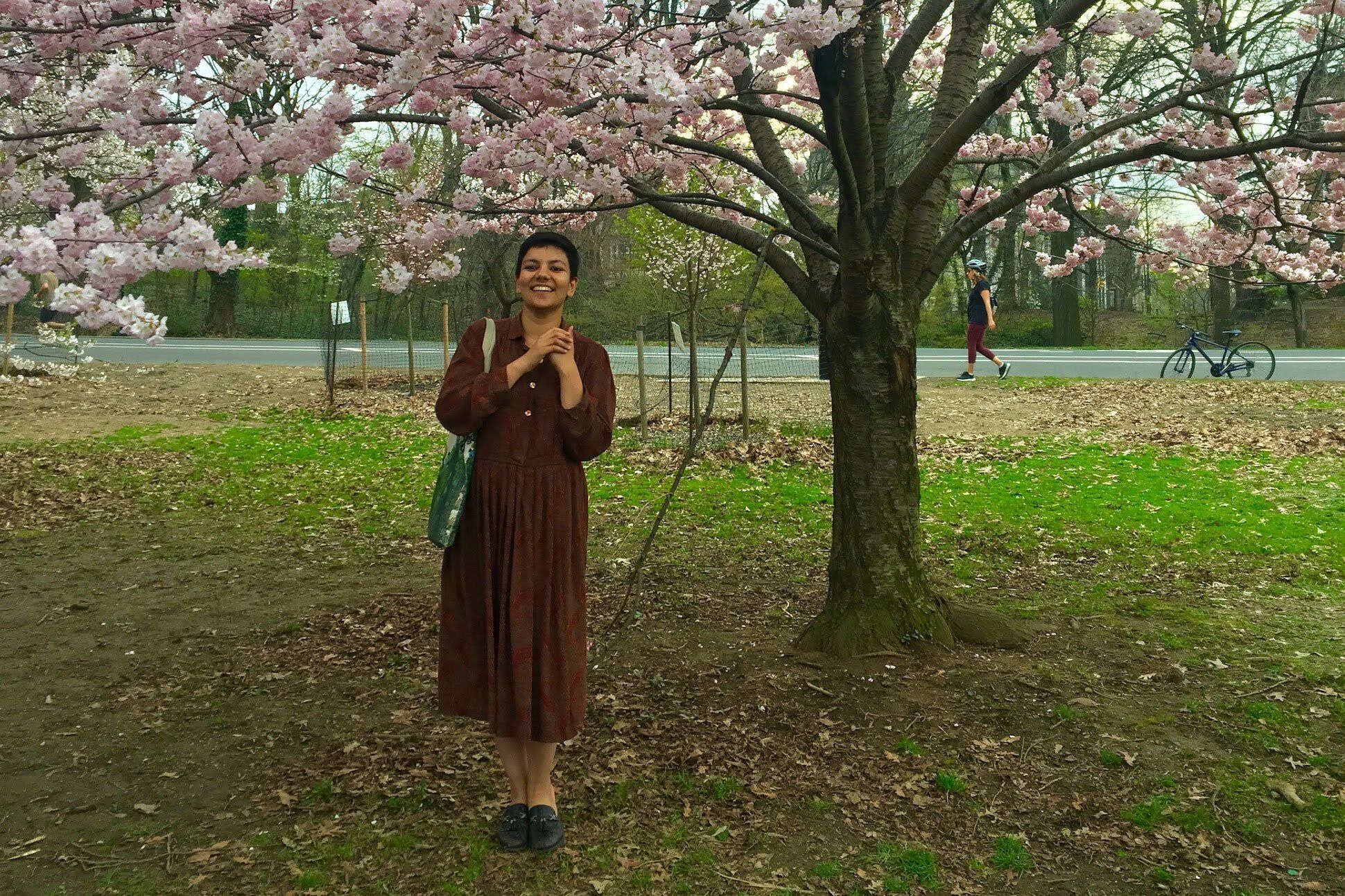 Short haired woman with dark red dress standing in front of a cherry blossom tree