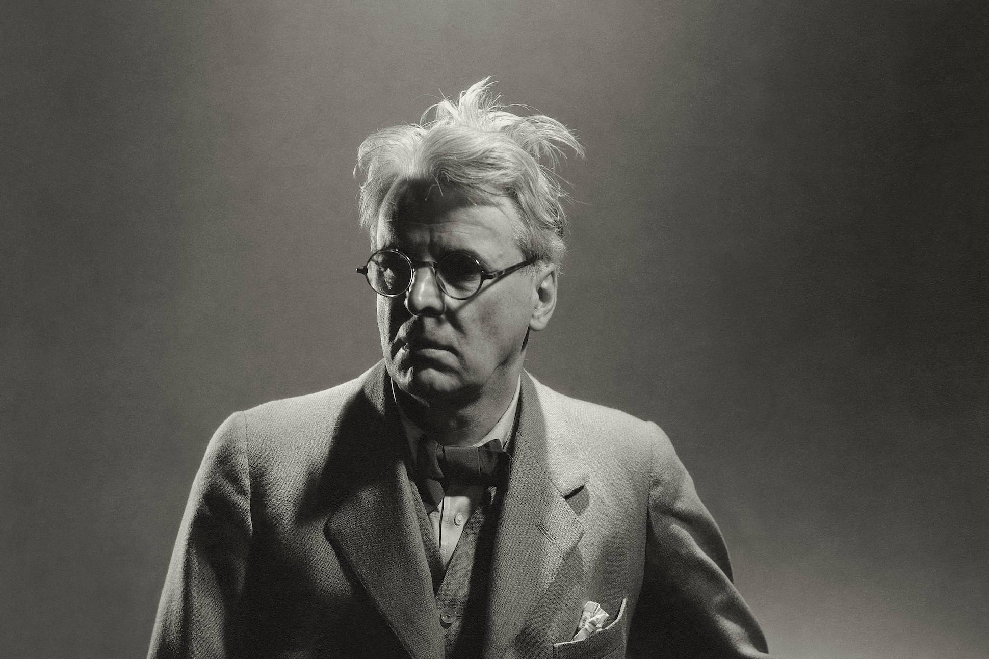 Irish poet William Butler Yeats wearing a light three-piece suit with a dark bow tie, and horn-rimmed glasses. (