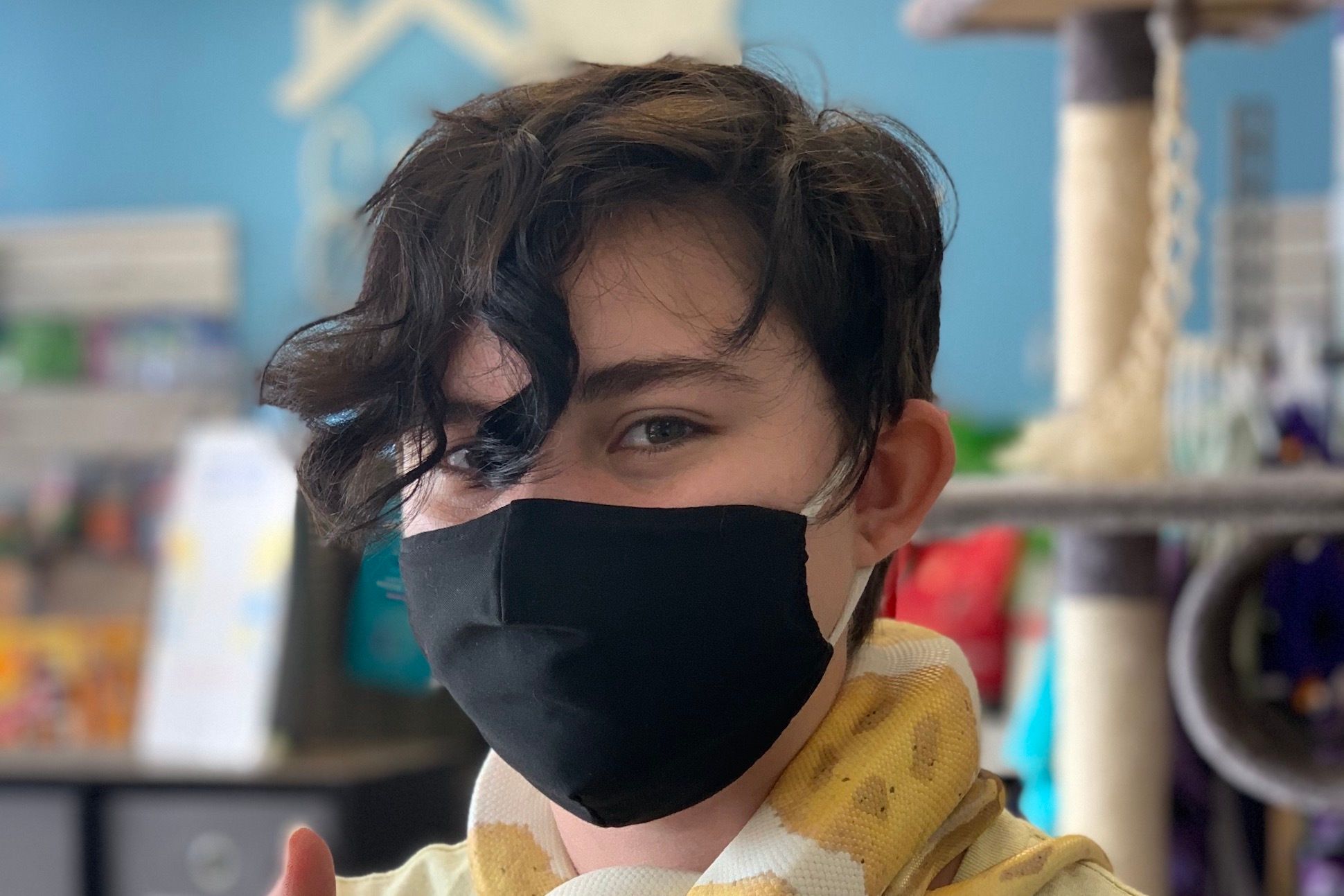 A short-haired male with a black fabric mask on his face and a yellow snack on his neck