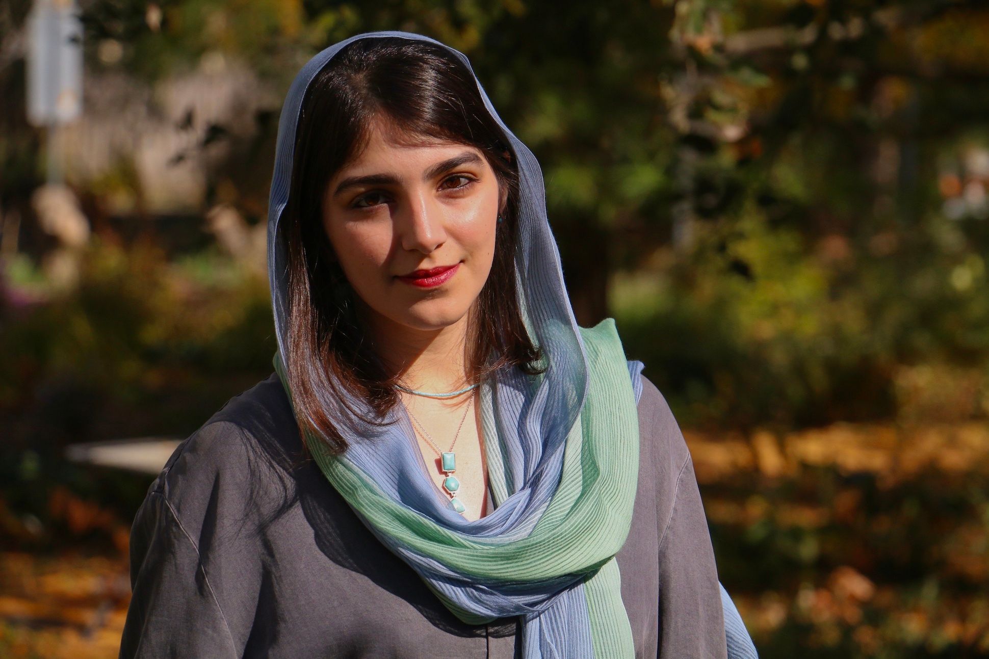 A woman wearing a hijab with dusty blue and turquoise smiling.