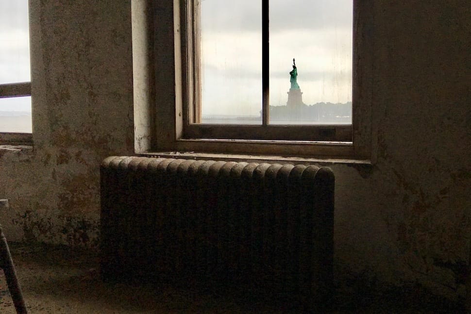 Photograph of the Statue of Liberty taken from the inside of a rustic room.