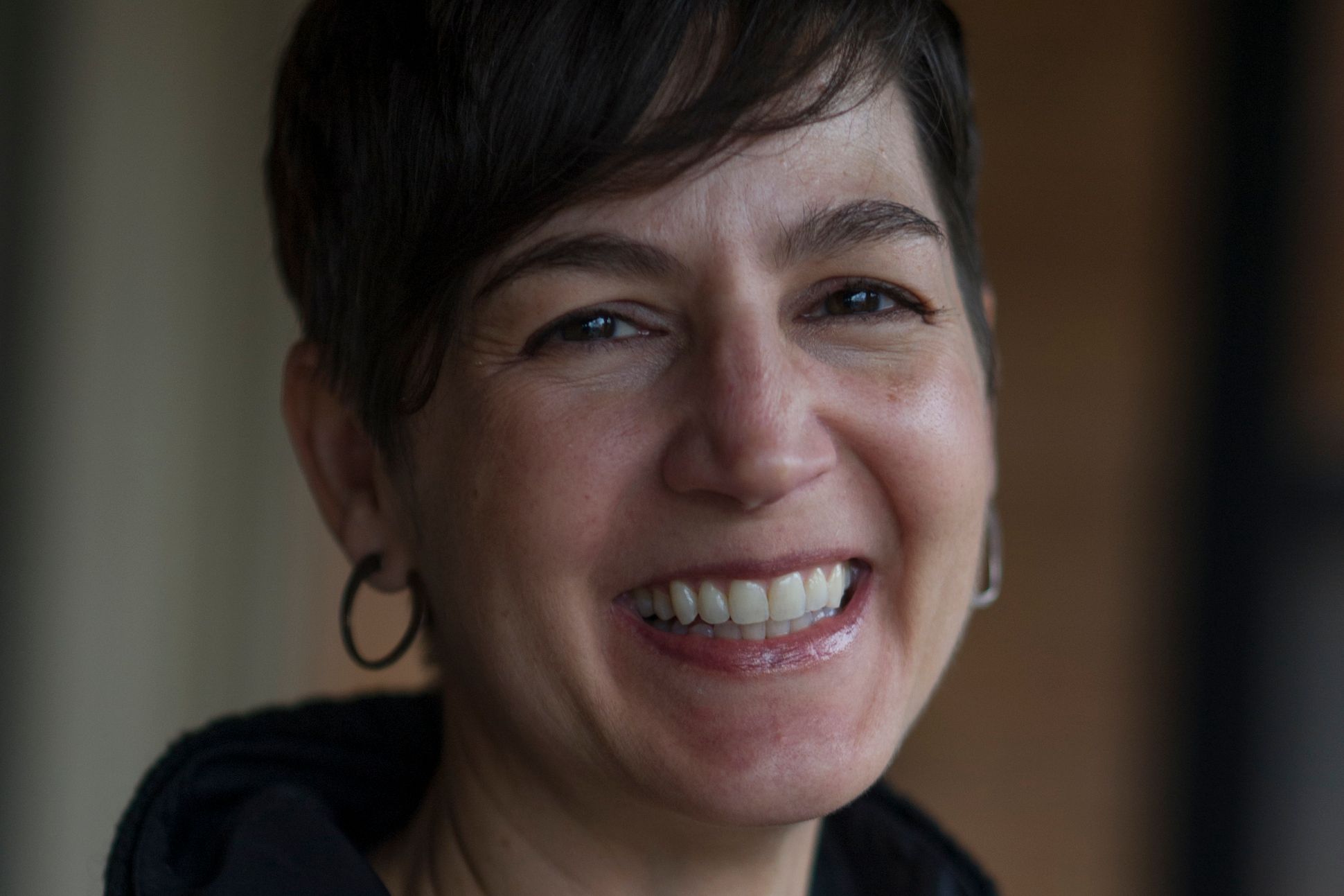 A short-haired woman with looped earrings smiling