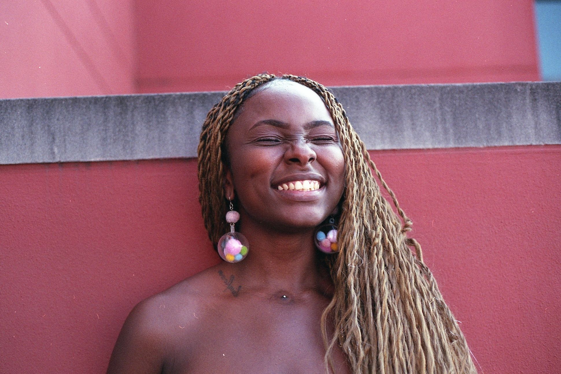 Kush Thompson, a black woman with golden blonde twists, smiles with her eyes closed in front of a red wall.