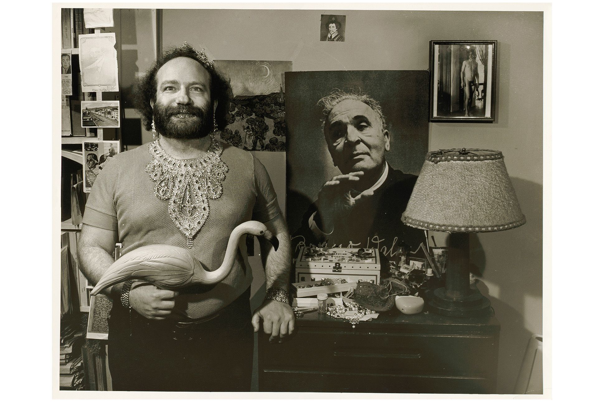 Black and white photo of David Menlick beside a dresser with a lamp and photographs along the wall, including a large photo of Bruno Walter.