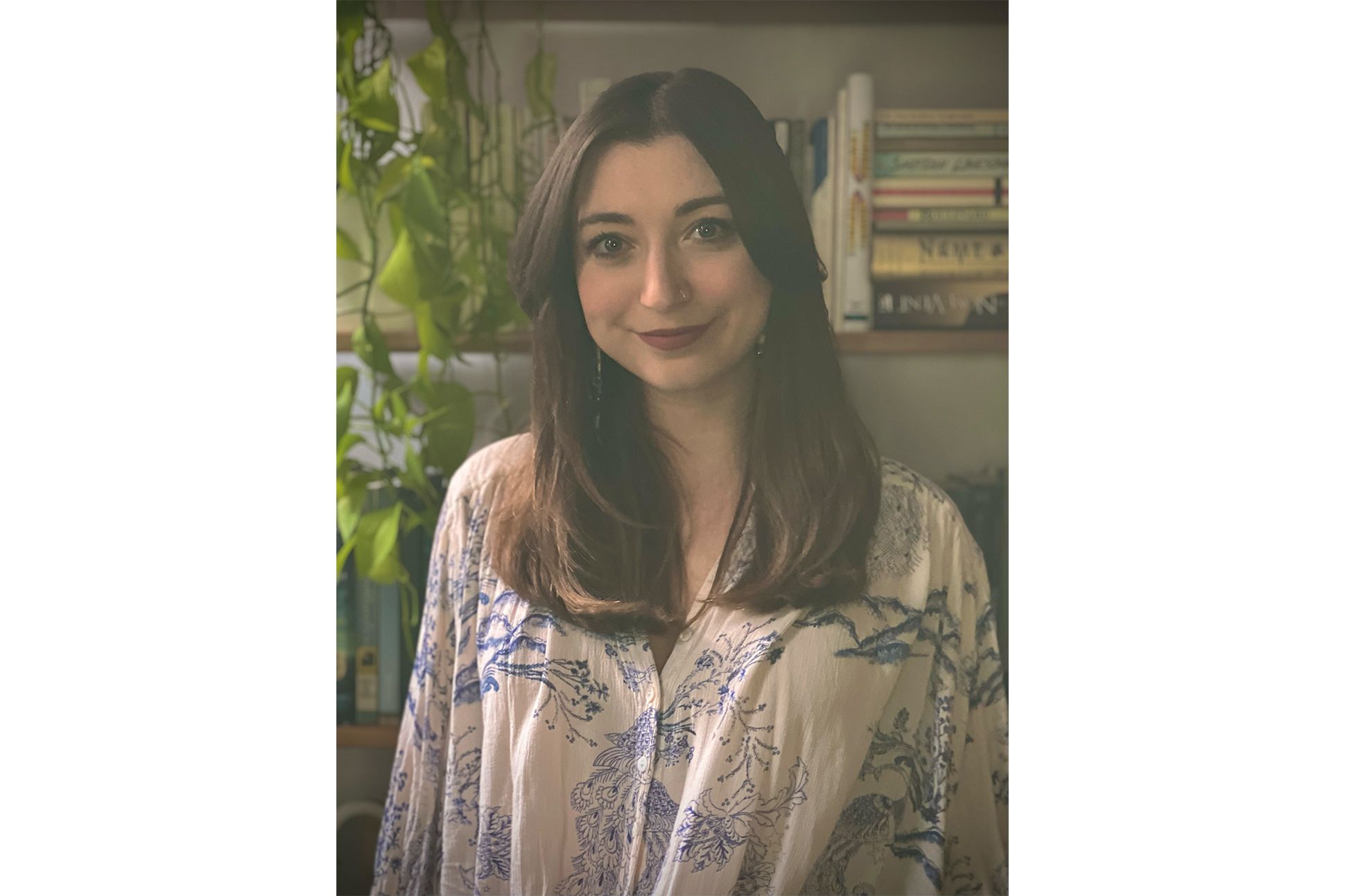 Natalia Conte, a brunette woman in a billowy shirt, poses in front of a bookcase with a pothos plant