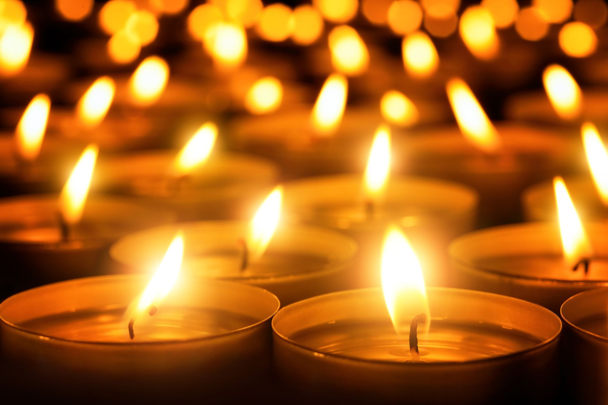 Image of many candle flames glowing in the dark.