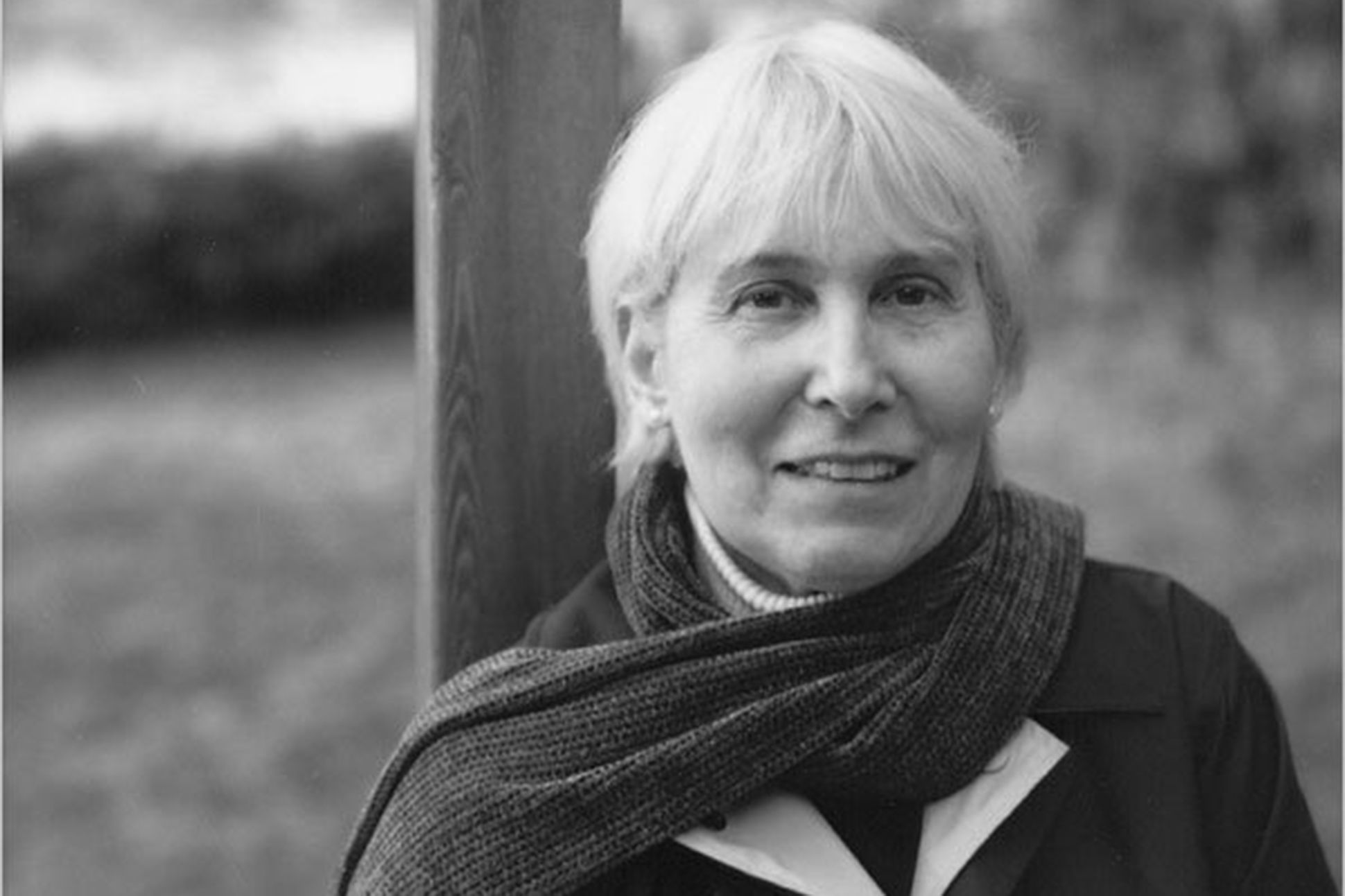 Black and white image of the children's poet Karla Kuskin in a scarf, leaning against a pole outside.