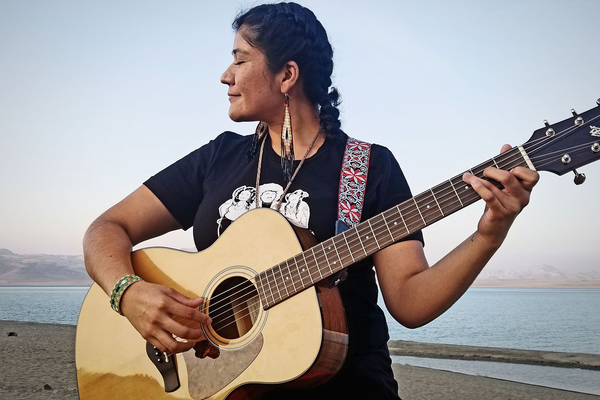 Poet Tanaya Winder playing an acoustic guitar on a beach