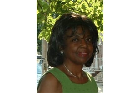 A black woman with short hair and a green dress in front of a tree