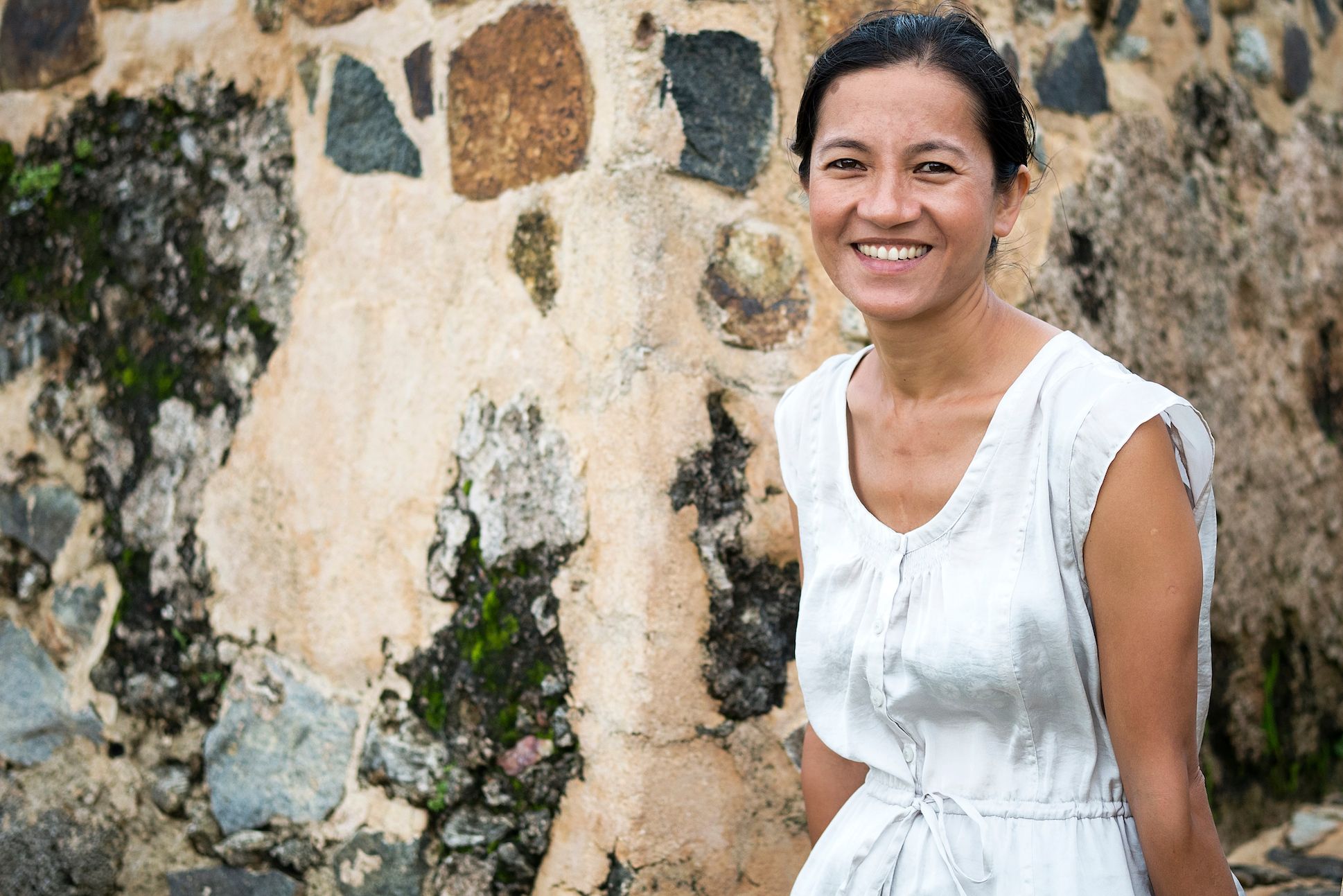 An Asian woman in a white dress sitting in front of a wall of mortars