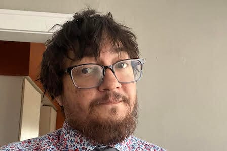 Selfie of a man with messy hair, glasses, and beard wearing a floral shirt