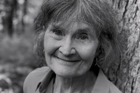 A black and white portrait of an elderly woman smiling in front of a tree