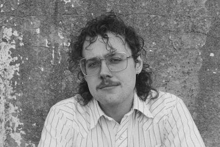 Black and white portrait of a man with long curly hair and glasses wearing a stripped shirt