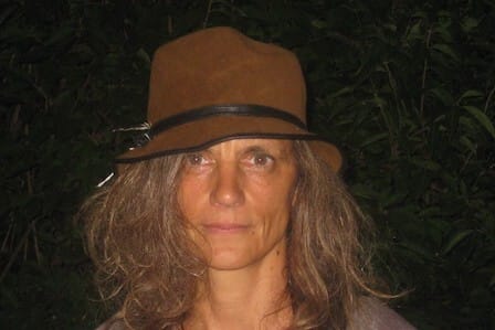 Woman with a hat smiling in front of a bush